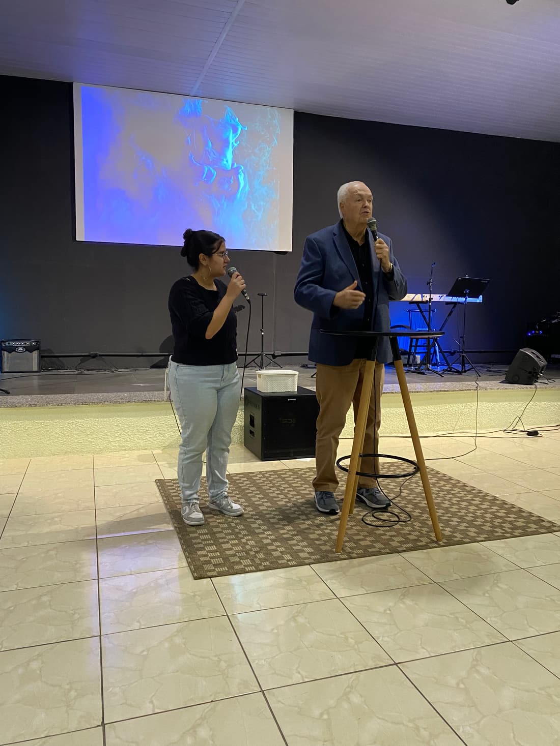 A man and a woman singing at the front of a hall during a conference opening in Brazil
